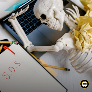 Skeleton with head laying on laptop and a notebook with S.O.S written on it to indicate that employee needs help.